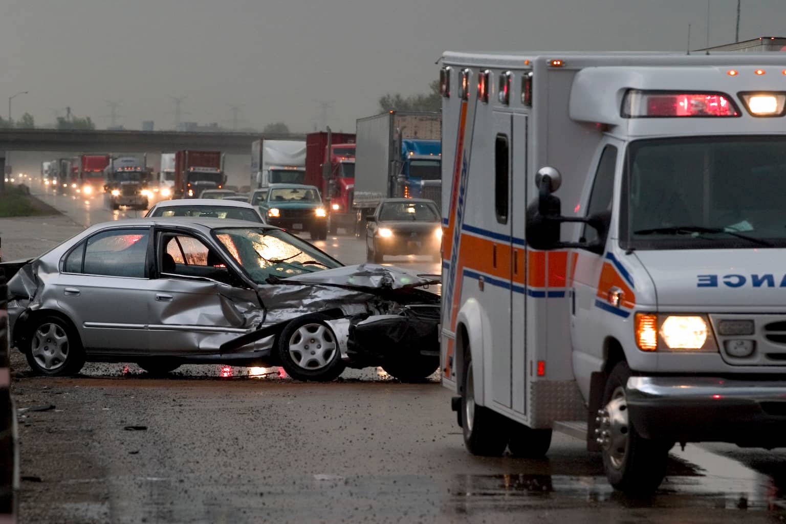 Car crash on major highway in Nashville during rainfall at night. Ambulance in foreground and police car in background.